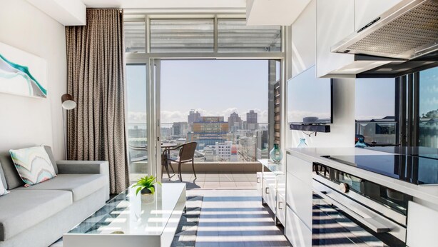 A modern living room with a sofa, coffee table, and a view of the city through large windows.