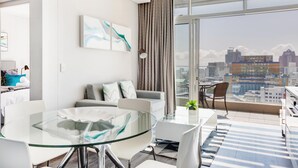 A modern living room with a glass table, grey sofa, and a city view through large windows.
