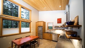 Une cuisine moderne avec des meubles en bois, un réfrigérateur en acier inoxydable, une cuisinière à gaz et un coin repas comprenant une table et des chaises en bois.