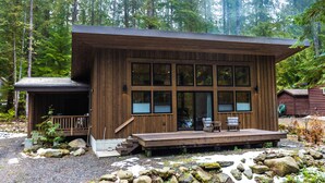 Une cabane en bois dotée d’une terrasse, de grandes fenêtres et d’un porche.