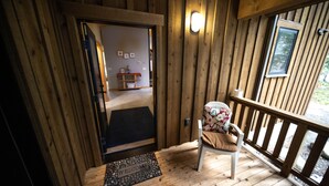 Une cabane en bois dotée d’une terrasse en bois, d’un banc et d’une chaise avec un coussin.