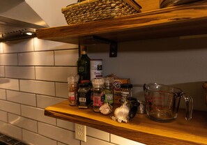 A kitchen shelf with various spices, a bottle of olive oil, a measuring cup, and a basket.