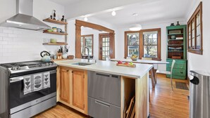 A modern kitchen with a central island, stainless steel appliances, wooden cabinets, and a view to the dining area. - Fulton Family Bungalow Pets Welcome. Crib, Highchair, Dog Crate (Minneapolis)