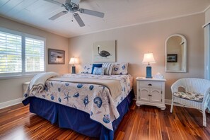 A bedroom with a bed, nightstands, a chair, a ceiling fan, and artwork on the walls.