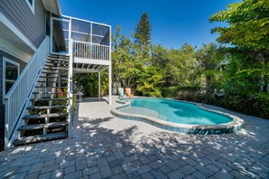 A residential backyard with a swimming pool, a staircase leading to a deck, and a variety of trees and plants. - Manatee Lookout (Anna Maria)
