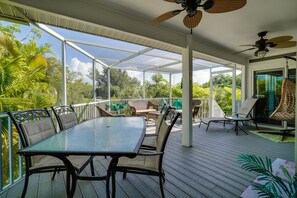 A covered outdoor area with a table and chairs, surrounded by lush greenery.