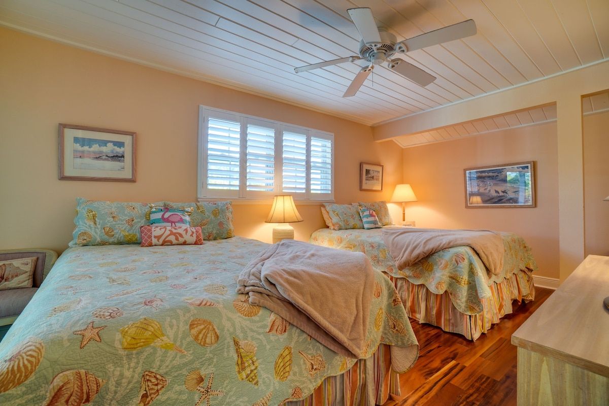 A bedroom with two beds, a ceiling fan, and artwork on the walls.