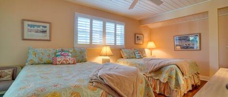 A bedroom with two beds, a ceiling fan, and artwork on the walls.