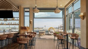 A modern bar area with high stools, a wooden bar counter, and a large window offering a city view. - AC Hotel by Marriott Columbus Downtown (Columbus)