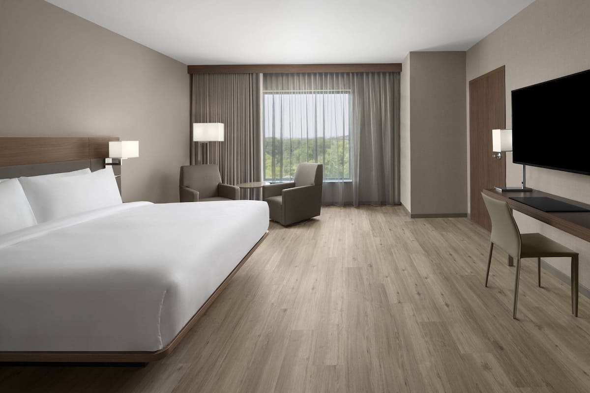 A hotel room with a large bed, a desk, a chair, a TV, and a window with curtains.