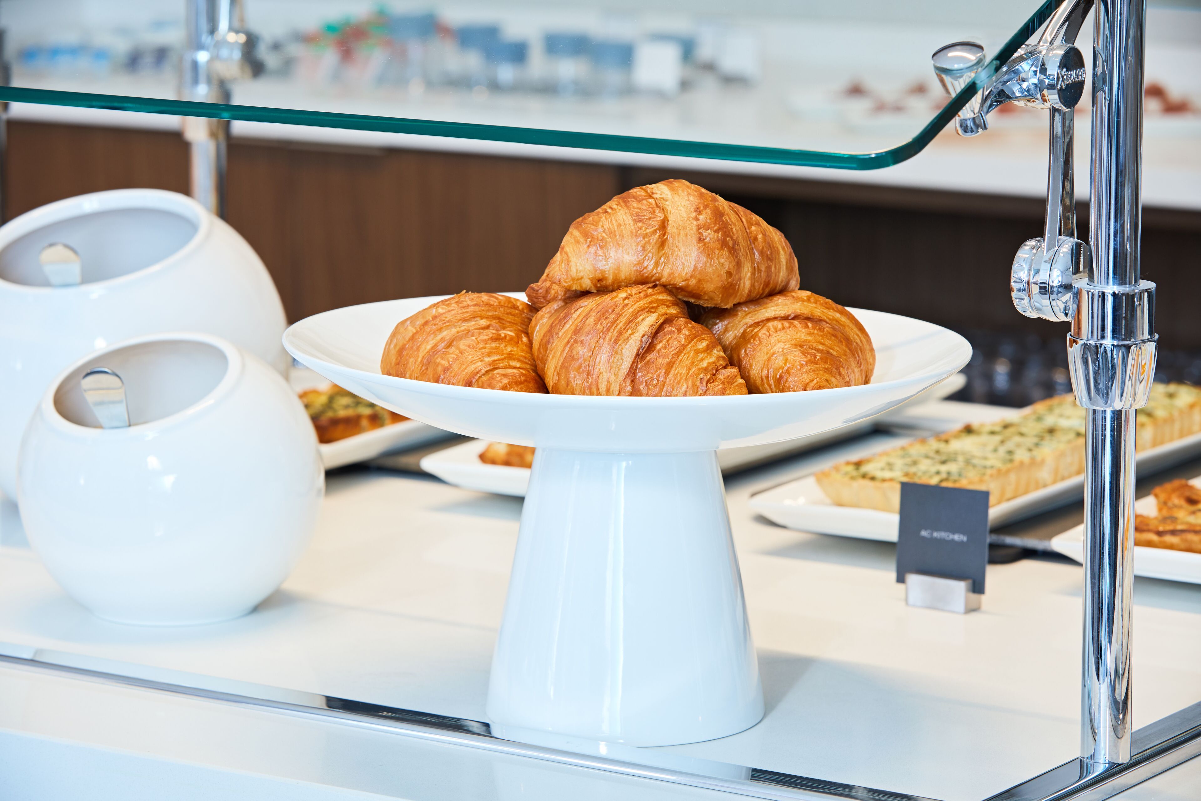 Croissanter anrettet på en hvid tallerken bag en glasbarriere i et bageri.