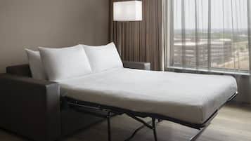 A modern hotel room with a bed, a bedside table, a lamp, and a view of the city through large windows.