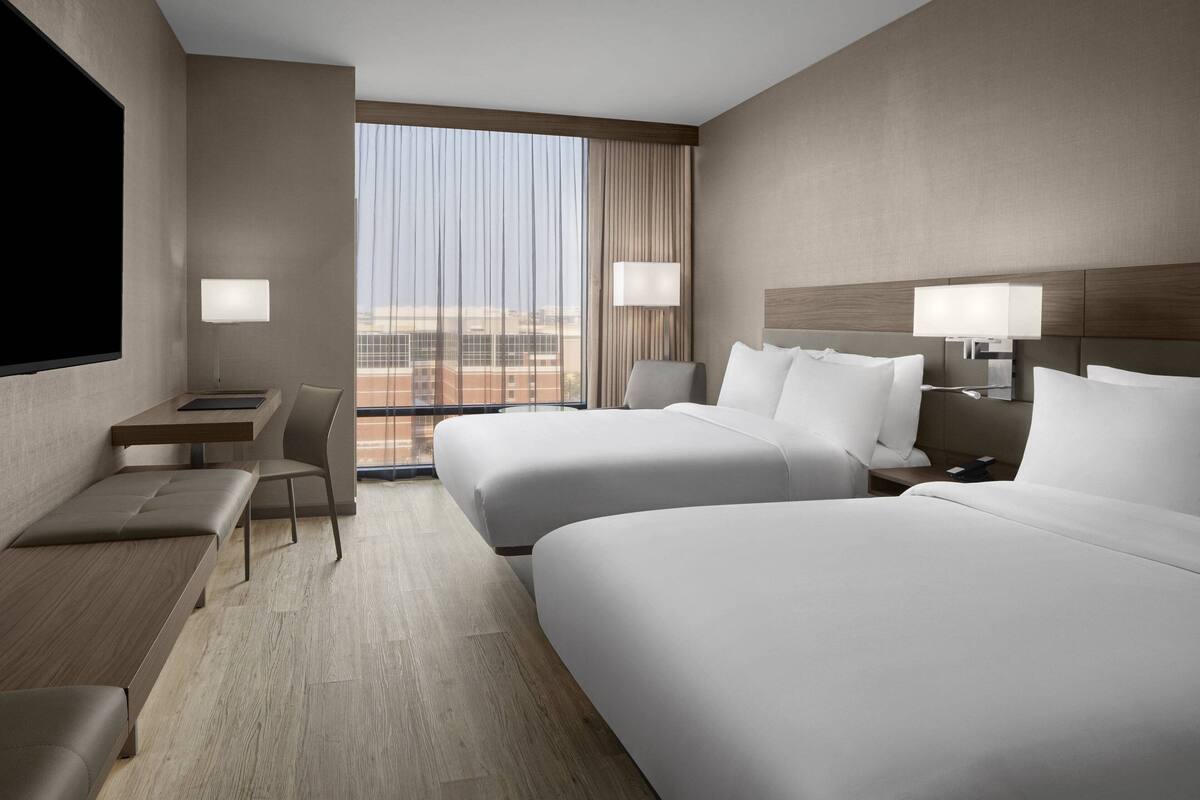 A hotel room with two beds, a desk, a chair, and a large window with a view.
