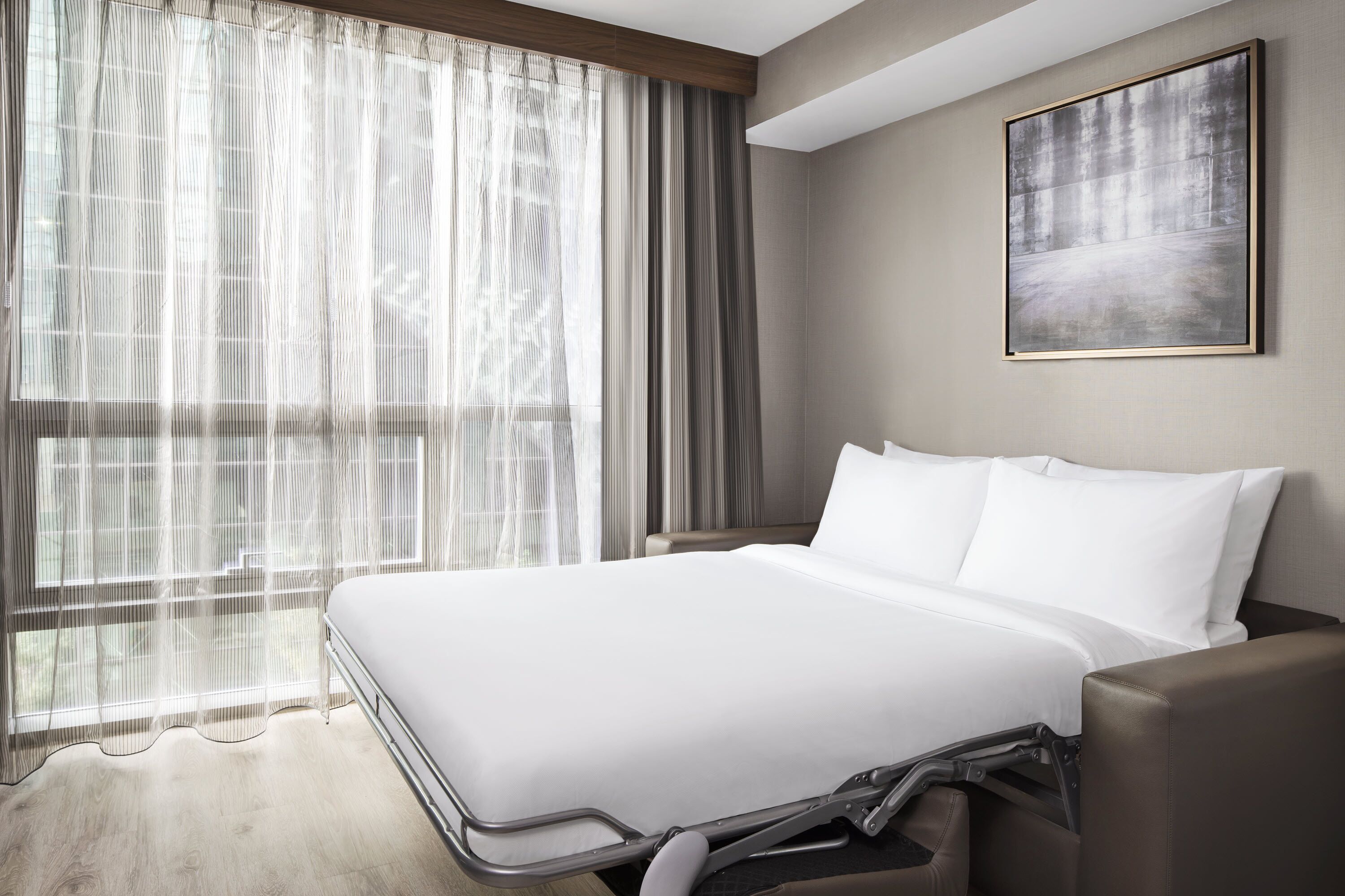 Un moderno cuarto de hotel con una cama grande, vistas a través de cortinas translúcidas, un cuadro en la pared y techo de madera.