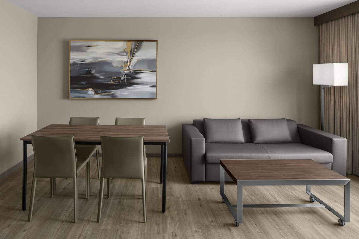 A modern hotel room with a dining table, chairs, a sofa, and a lamp.