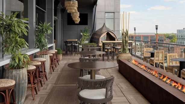 A rooftop bar with wicker furniture, a fire feature, and a view of the city. - AC Hotel by Marriott Columbus Downtown (Columbus)