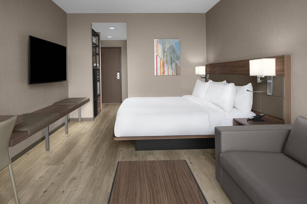 A modern hotel room with a large bed, a flat-screen TV, a desk, and a sofa.
