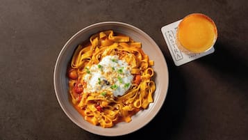 Un plato de pasta con un aderezo cremoso y un vaso pequeño de jugo de naranja sobre una mesa.
