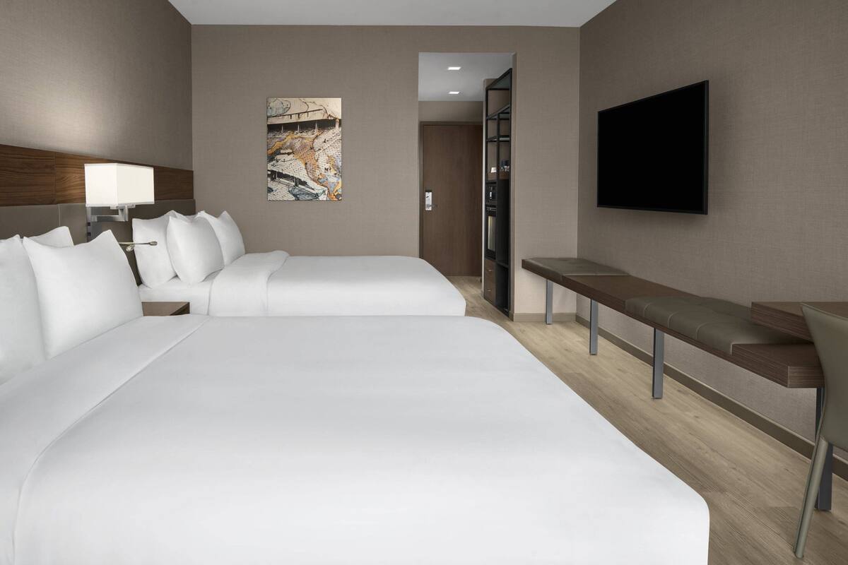 A hotel room with two beds, a TV, a desk, and a painting on the wall.