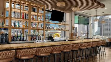 A bar area with wooden shelves, stools, and a large screen.