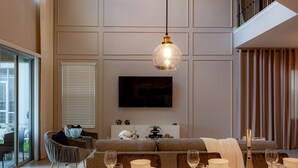 A modern living room with a dining area, a flat-screen TV mounted on the wall, and a staircase leading to an upper level. - 801DSD: Stunning 5 Bedroom Villa - Private Pool and Spa with Nature View (Kissimmee)