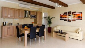 A modern kitchen with wooden cabinets, a dining table with chairs, a microwave, and a potted plant. - Misrah Simar (Qala)