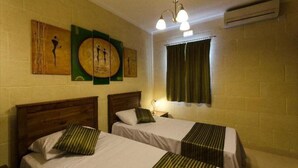 A hotel room with two single beds, a wooden headboard, a green curtain, and artwork on the wall. - Misrah Simar (Qala)
