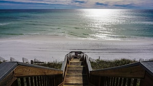 Ein hölzerner Promenadenweg führt zu einem Strand mit Blick auf das Meer und einen bewölkten Himmel.