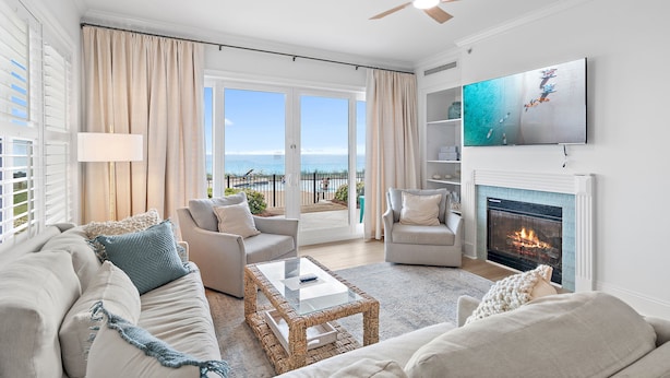 Ein Wohnzimmer mit Sofa, Sesseln, Couchtisch, Kamin, Fernseher und einem Balkon mit Aussicht.