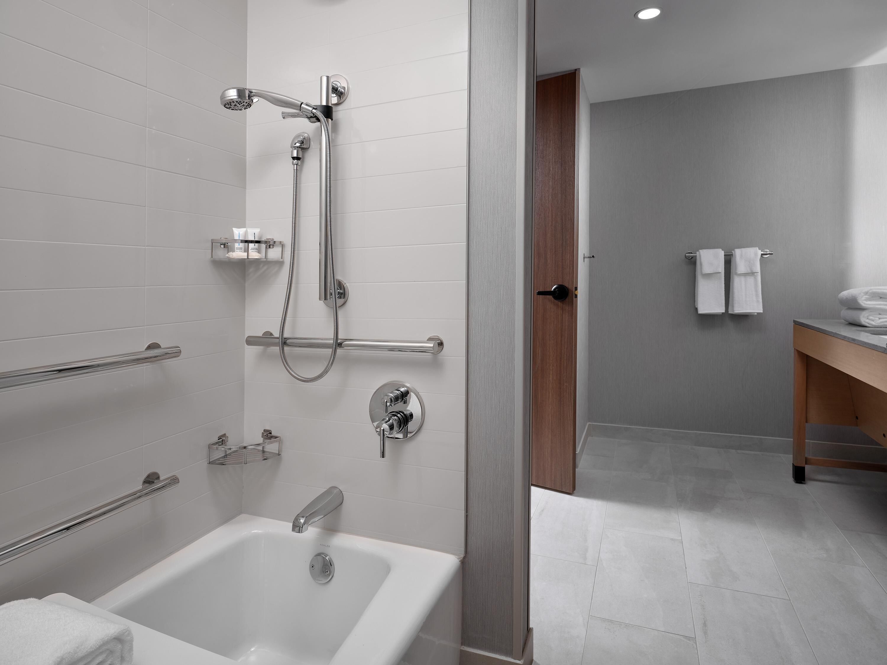 A modern bathroom with a bathtub, shower, and handrail.