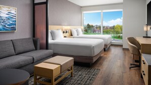 A modern hotel room with a sofa, two beds, a desk, and a large window offering a view of the outdoors. - The Forester Hotel, part of Unscripted by Hyatt (Lake Forest)