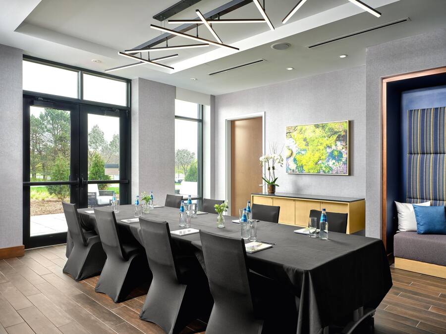 Een moderne vergaderruimte met een lange tafel, stoelen, een bank en een groot raam.