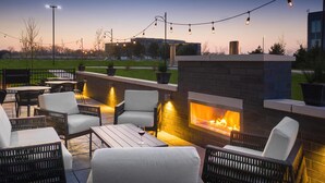 An outdoor patio with wicker furniture, a brick fireplace, and string lights. - The Forester Hotel, part of Unscripted by Hyatt (Lake Forest)