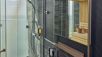A modern bathroom with a glass shower enclosure, a wooden bench, and a large mirror reflecting a sauna area.