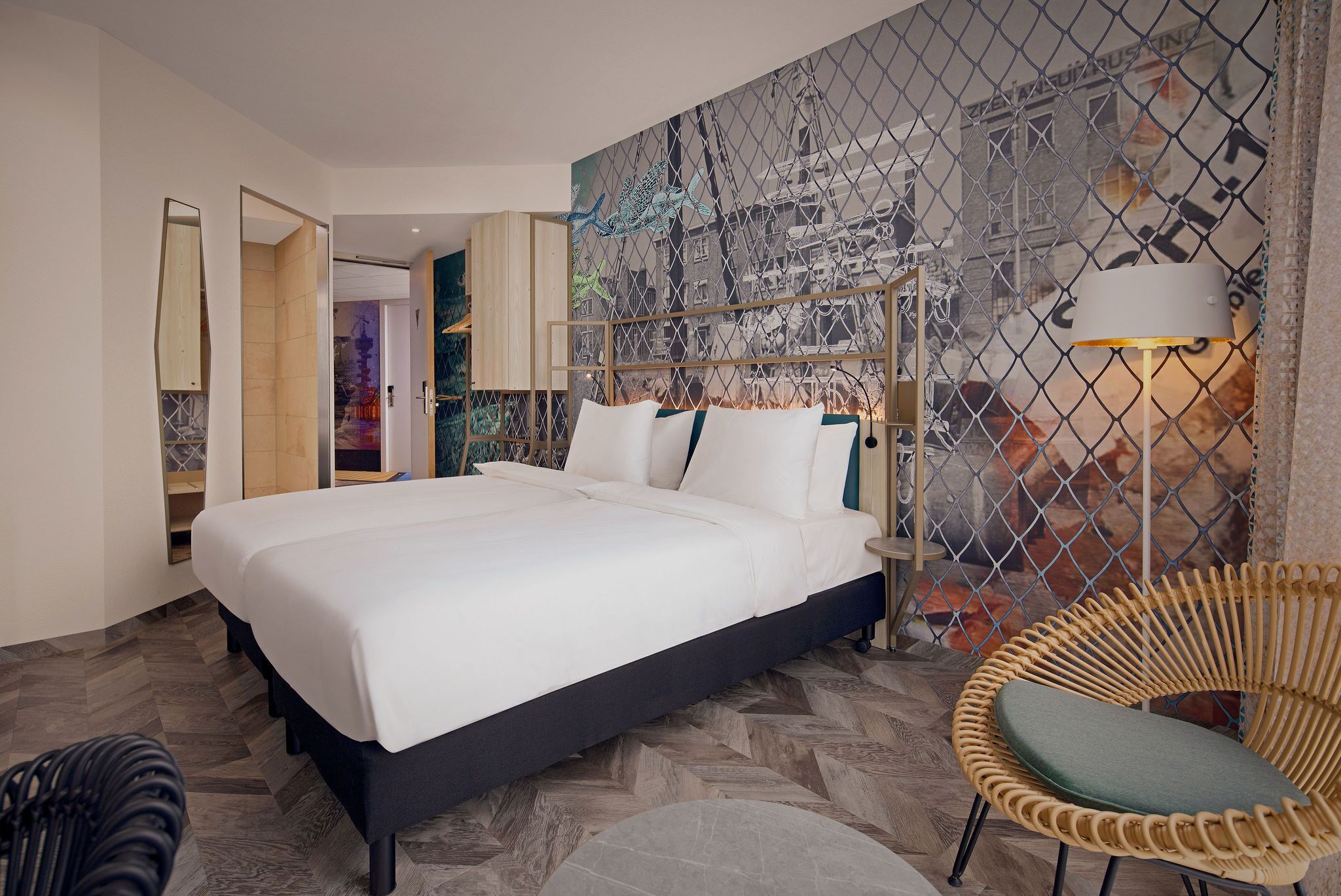 Quarto de hotel moderno com uma cama grande, uma cadeira de vime e um mural com vista para a cidade na parede.