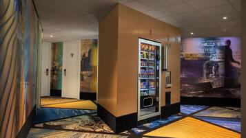 A hotel lobby with a vending machine, a large digital screen, and a patterned floor.