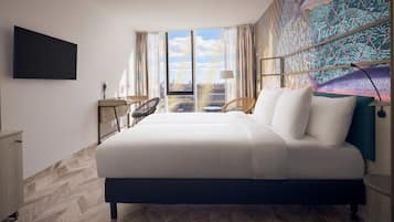 A hotel room with a large bed, a flat-screen TV mounted on the wall, a view of the city through large windows, and a patterned tapestry on the wall.