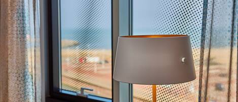 A lamp with a white shade and a switch, positioned near a window with a view of a beach.
