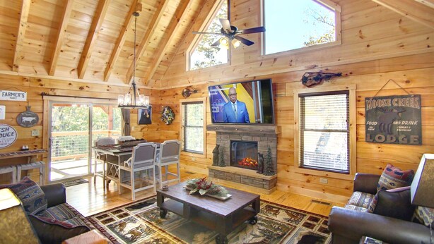 Eine geräumige Holzhütte mit hoher Decke, Kamin, Fernseher und Essbereich.