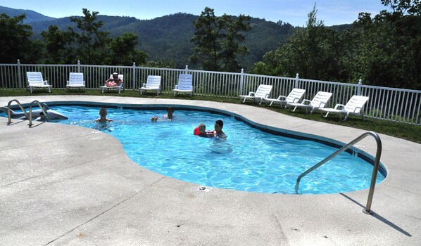 A swimming pool with a view of mountains, surrounded by white lounge chairs and a white fence.