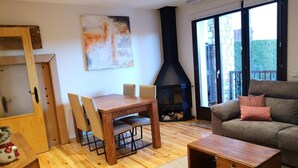 A living room with a wooden dining table, chairs, a sofa, a fireplace, and a large window.