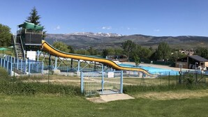 A playground with a yellow slide, a pool, and mountains in the background.