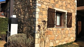 A stone building with a window and shutters, a small plant, and a concrete structure.