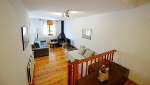 A room with a wooden floor, a sofa, a dining table, a fireplace, and a TV.