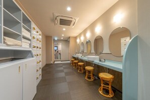 Bagno d'hotel con più lavandini, sgabelli in vimini e un'area contenitiva con cassetti e mensole.