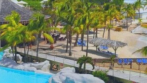 Un resort con piscina, palmeras, sombrillas de playa y vista al océano.