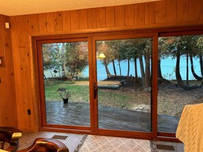 A room with wooden paneled walls, a large sliding glass door leading to an outdoor deck with a view of trees and a body of water.