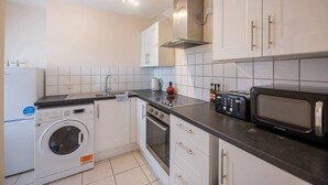 A compact kitchen with a washing machine, oven, microwave, and white cabinets.