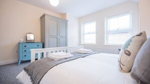 A bedroom with a bed, a dresser, a wardrobe, and two windows.