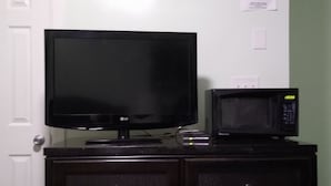 A flat-screen TV and a microwave on a dark wooden cabinet. - Laurel Notch Motel (Bordentown)